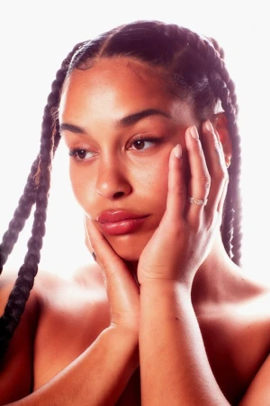 Close-up portrait of a woman with braided hair holding her face in her hands against a bright white background