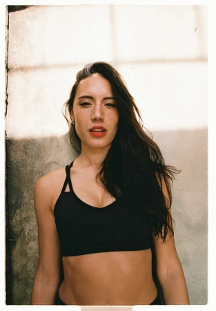 Portrait of a woman with dark hair wearing a black sports bra against a textured background by Danika Magdelena