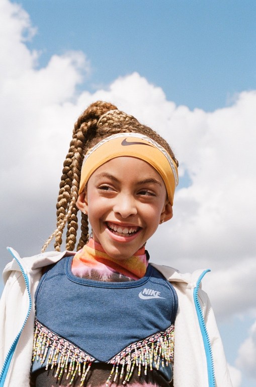 Smiling child wearing a headband and athletic wear against a sunny sky with scattered clouds. A joyful portrait of youth.