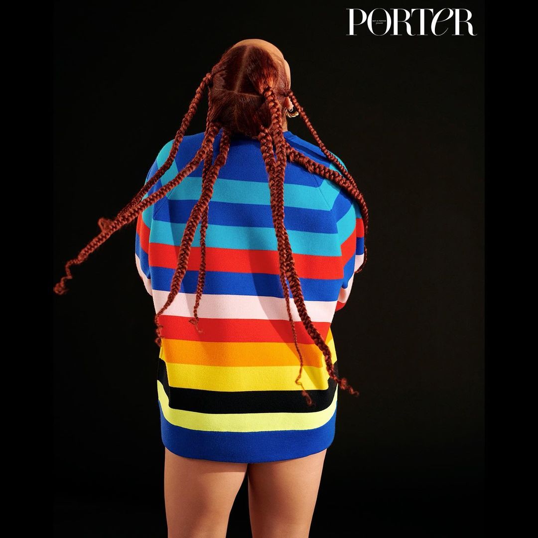 Fashion shot of a woman with braids in a colorful striped sweater on a black backdrop, showcasing a modern and stylish look.