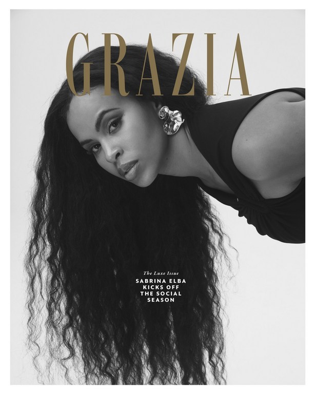 Monochrome magazine cover portrait of Sabrina Elba with long dark wavy hair wearing statement earrings.