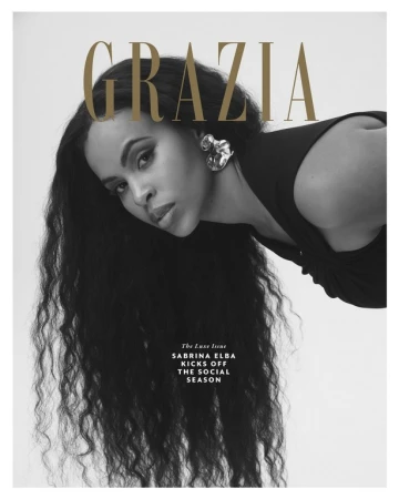 Monochrome magazine cover portrait of Sabrina Elba with long dark wavy hair wearing statement earrings.