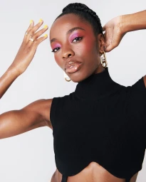 Black woman with pink eyeshadow wearing a black ribbed sleeveless top and gold earrings, photographed by Danika Magdelena