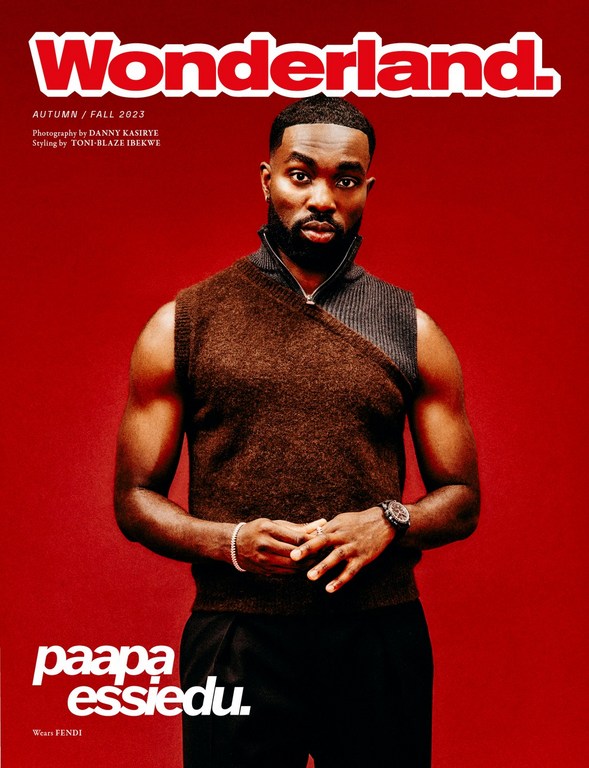 Paapa Essiedu on the cover of Wonderland Autumn/Fall 2023, wearing a brown knit vest against a red backdrop, captured in a medium shot.