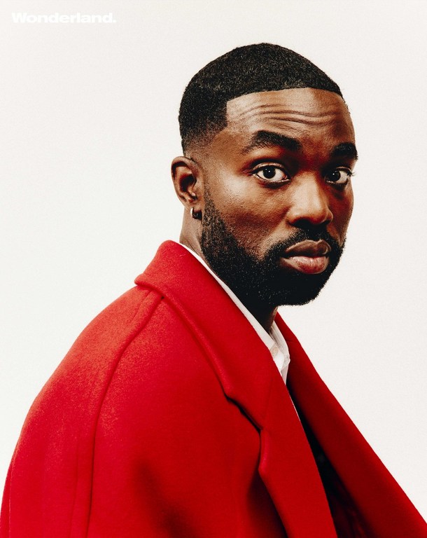 Portrait of an African American male model in a red overcoat against a white background for Wonderland magazine, showcasing sharp grooming.