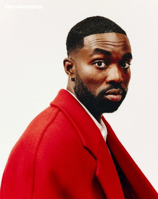 Portrait of an African American male model in a red overcoat against a white background for Wonderland magazine, showcasing sharp grooming.