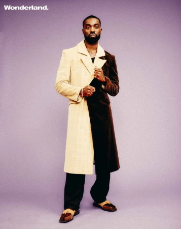 Black man wearing a split-color beige and brown trench coat standing against a purple background by Danny Kasirye