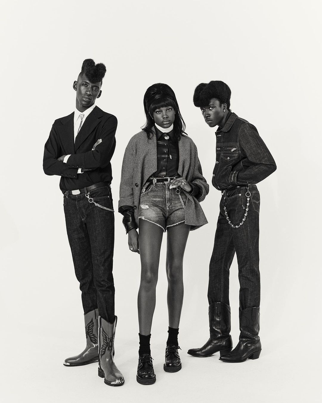 Three young African-descent fashion models in vintage-inspired attire against a light background, showcasing style and unique hairstyles.