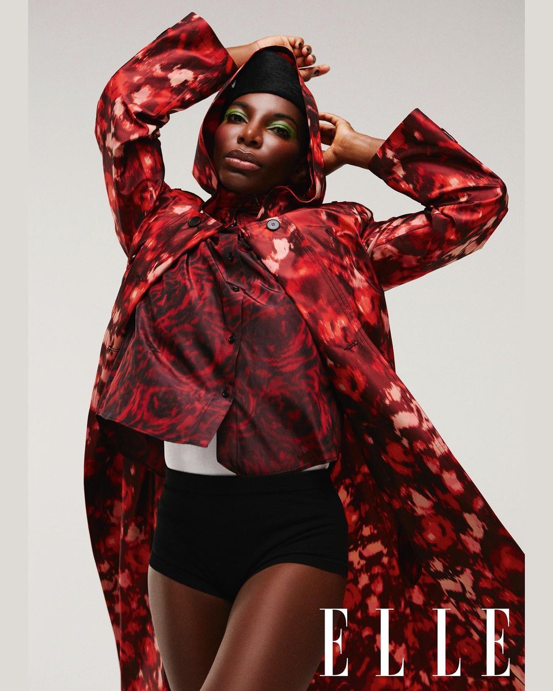 A fashionable portrait of a black woman in a hooded jacket, paired with a top and black shorts, set against a plain backdrop. ELLE logo.