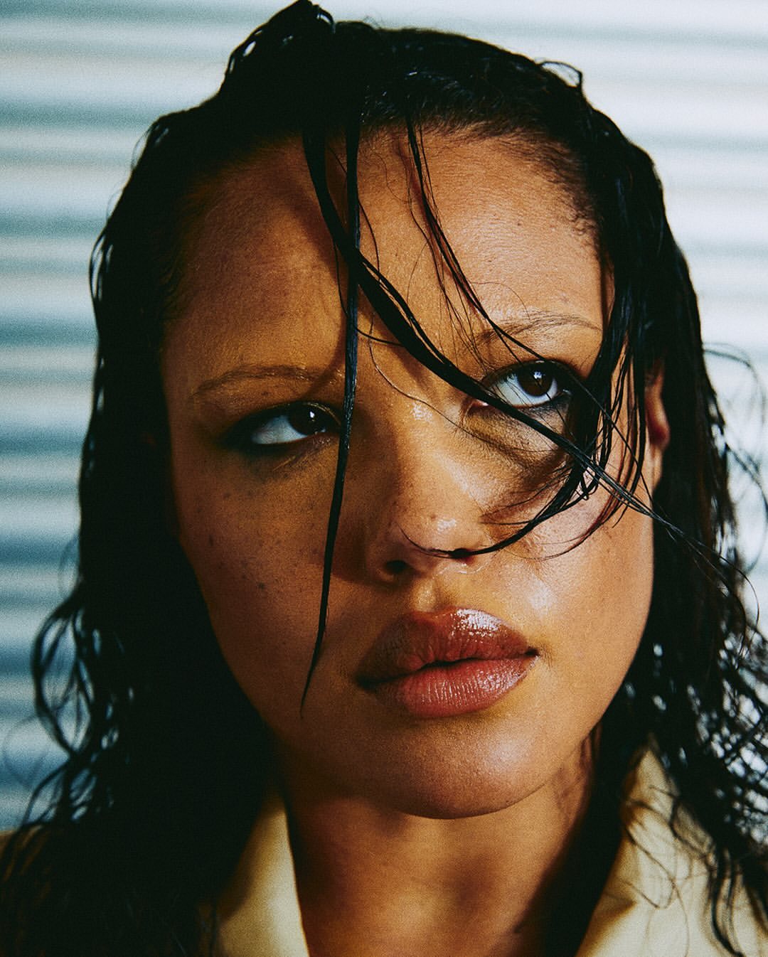 Close-up portrait of a woman with wet dark hair clinging to her face, glancing upwards with a serious expression.