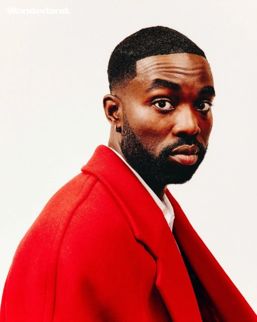 Portrait of a stylish African-American man with a beard, wearing a red coat against a bright background, showcasing a blend of fashion and elegance.