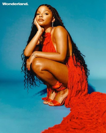 Halle Bailey crouching in a vibrant red dress against a bright blue studio backdrop photographed by Danny Kasirye.