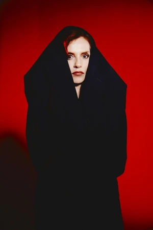 Striking portrait of a woman with red hair wrapped in black fabric against a bold red backdrop, creating a dramatic and mysterious atmosphere.