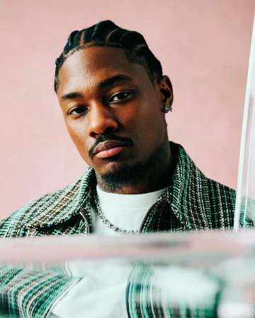 Portrait of a Black man with braided hair wearing a patterned green jacket and white t-shirt by photographer Danny Kasirye.