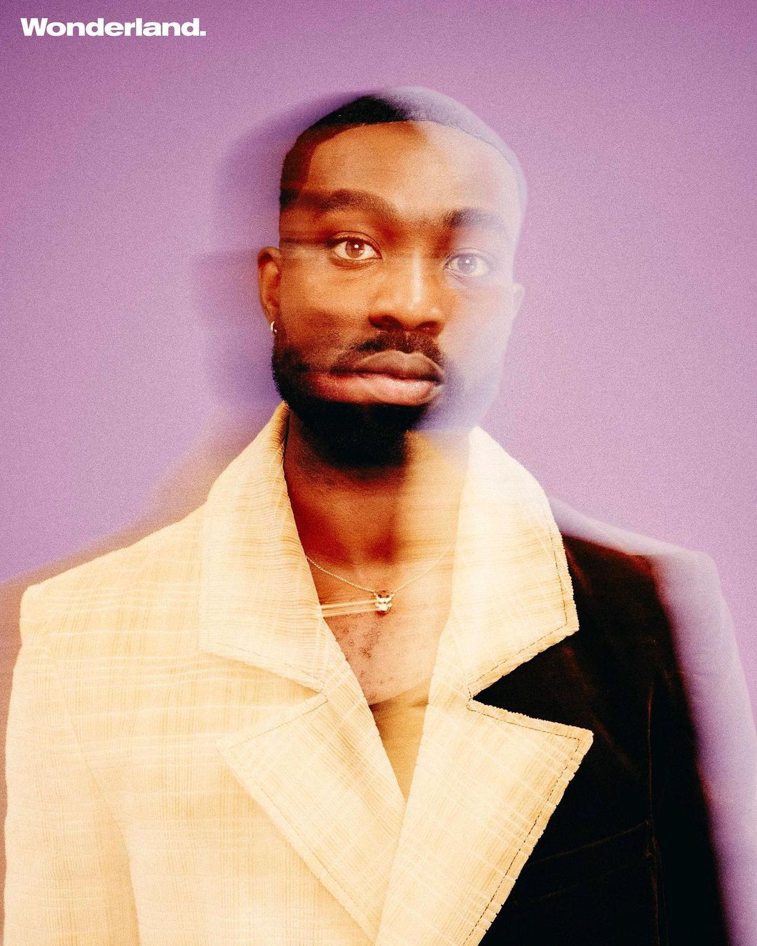 Portrait of a Black man in a two-tone blazer against a purple backdrop for Wonderland magazine, showcasing modern fashion and style.