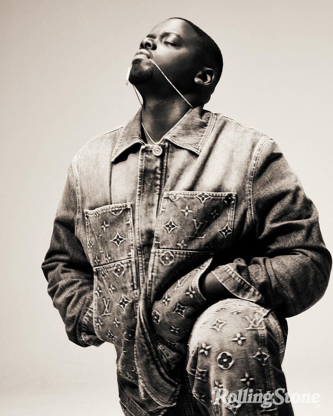 A man poses in a denim Louis Vuitton jacket and pants with his head tilted back, looking up, and against a light neutral background.
