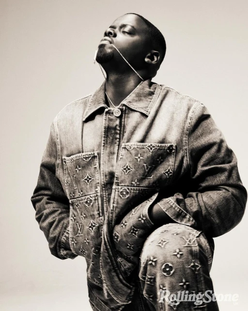 A man poses in a denim Louis Vuitton jacket and pants with his head tilted back, looking up, and against a light neutral background.