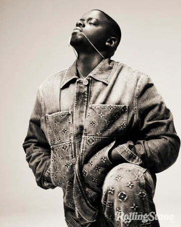 A man poses in a denim Louis Vuitton jacket and pants with his head tilted back, looking up, and against a light neutral background.