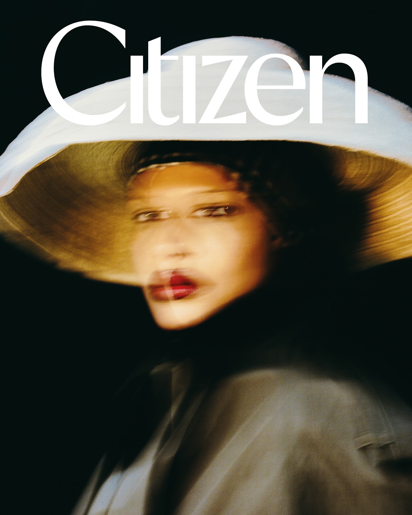Portrait of a woman wearing a wide-brimmed white hat and dark clothing against a dark background, captured with motion blur.