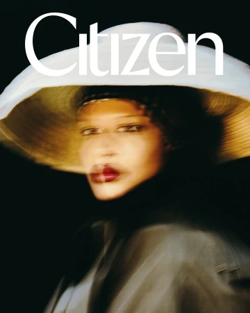 Portrait of a woman wearing a wide-brimmed white hat and dark clothing against a dark background, captured with motion blur.