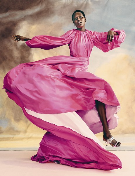 Woman in a flowing pink gown strikes a pose against a painterly background. The garment dominates the scene with dynamic movement.
