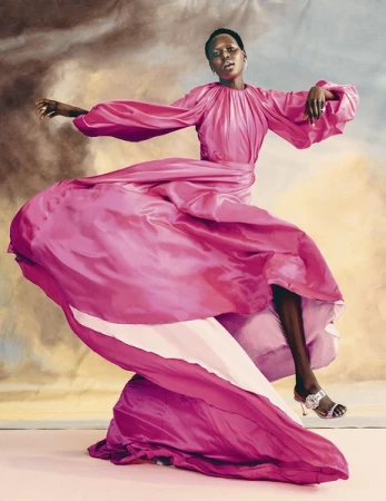 Woman in a flowing pink gown strikes a pose against a painterly background. The garment dominates the scene with dynamic movement.