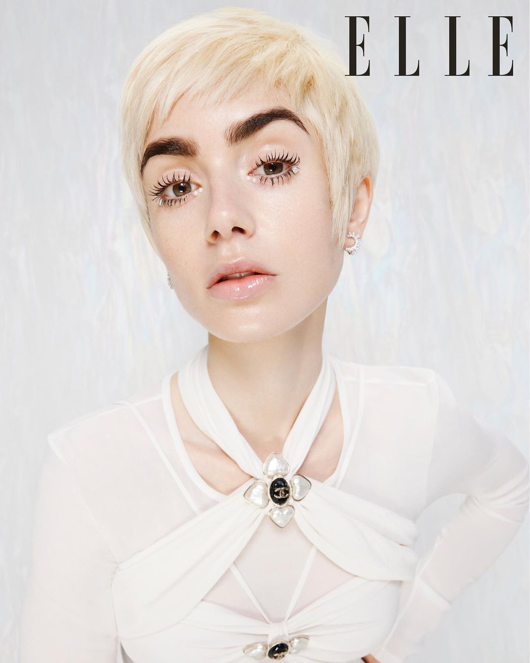 Close-up portrait of a blonde woman with bold eyebrows in a white top, with the 'ELLE' magazine logo in the upper-right corner.