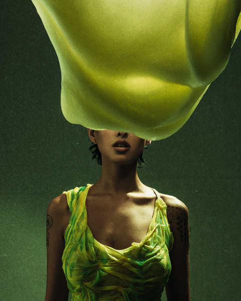 Woman in a bright green top with a large yellow-green organic form over her head against a green background in a studio shot.
