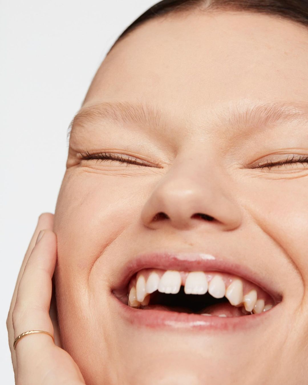 Close-up shot of a smiling adult woman with light skin, showing her teeth and a small gap between her front teeth, indoor on white backdrop.