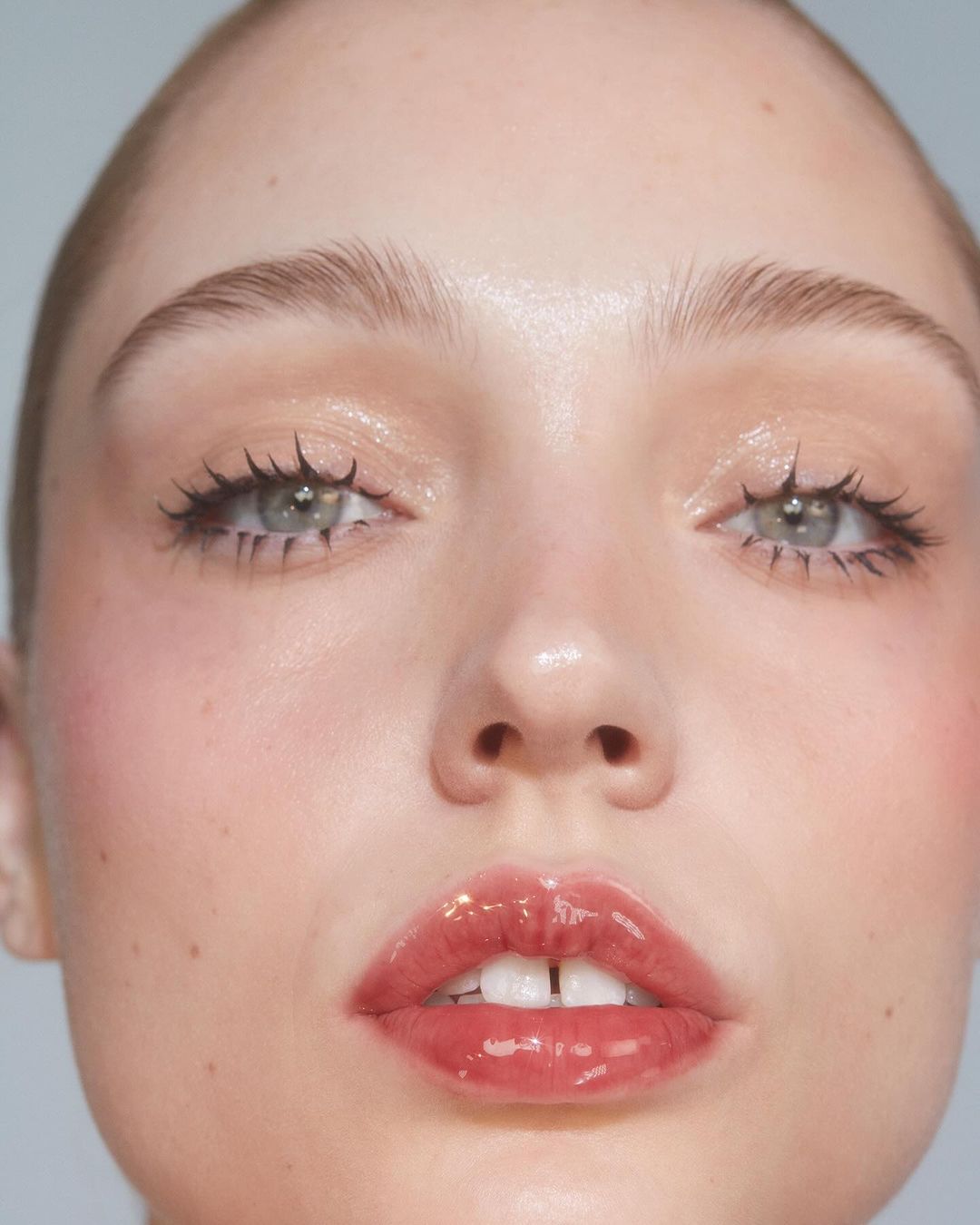 Close-up beauty shot of a fair-skinned woman with glossy lips and shimmery eyeshadow against a neutral background. Focus on her facial features.