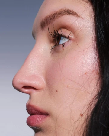 Close-up profile portrait of a woman's face showing her eye, nose, and lips against a plain neutral background.