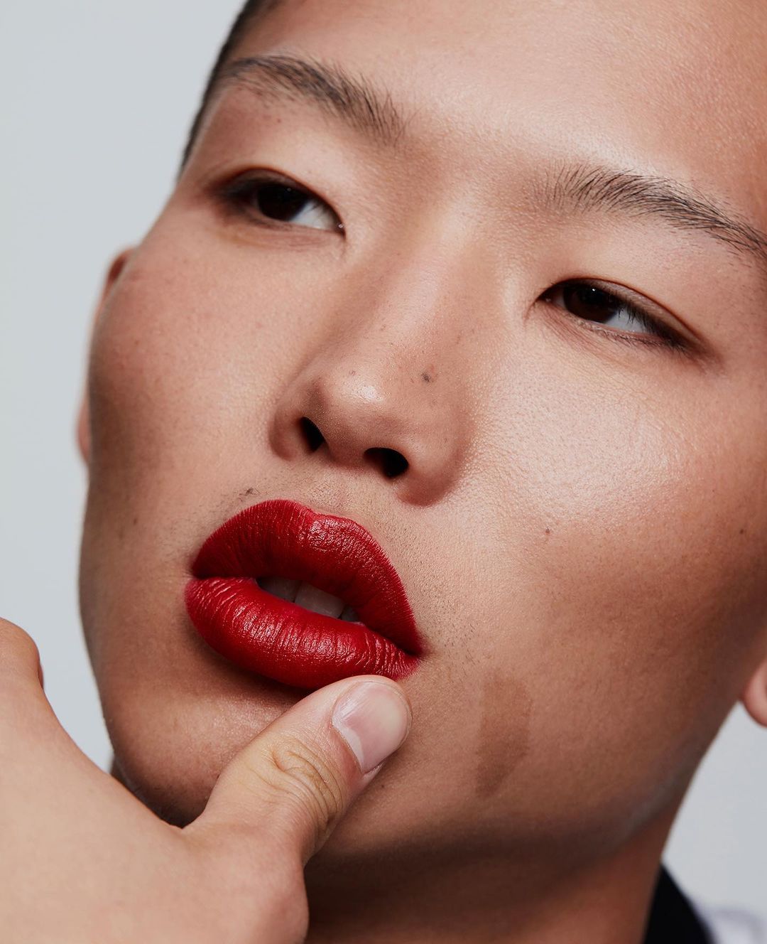Close-up portrait of a person with makeup, featuring red lipstick and clear skin, against a simple background in studio lighting.