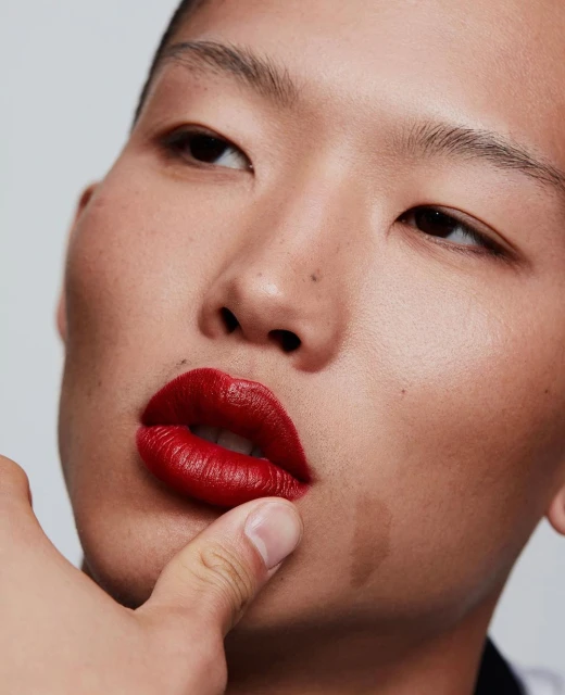 Close-up portrait of a person with makeup, featuring red lipstick and clear skin, against a simple background in studio lighting.