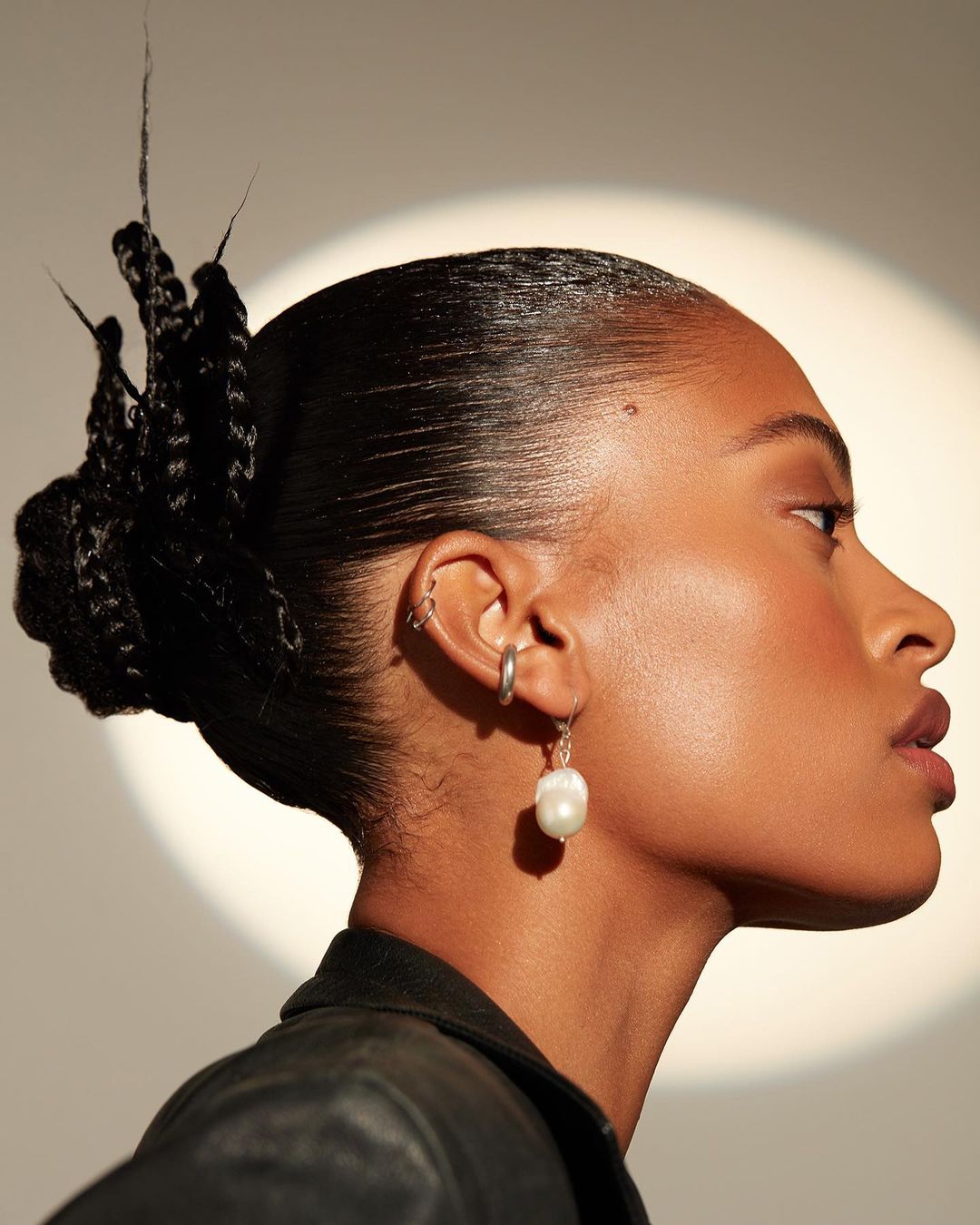 Profile shot of a black female model wearing pearl earring. The woman has slicked back black hair, with fair skin and soft lighting.