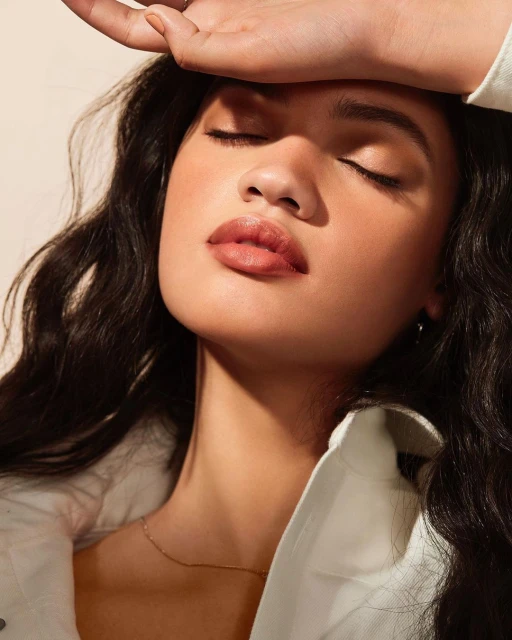 Close-up portrait of a young adult female with her eyes closed, illuminated by natural sunlight, wearing a white collared shirt indoors.