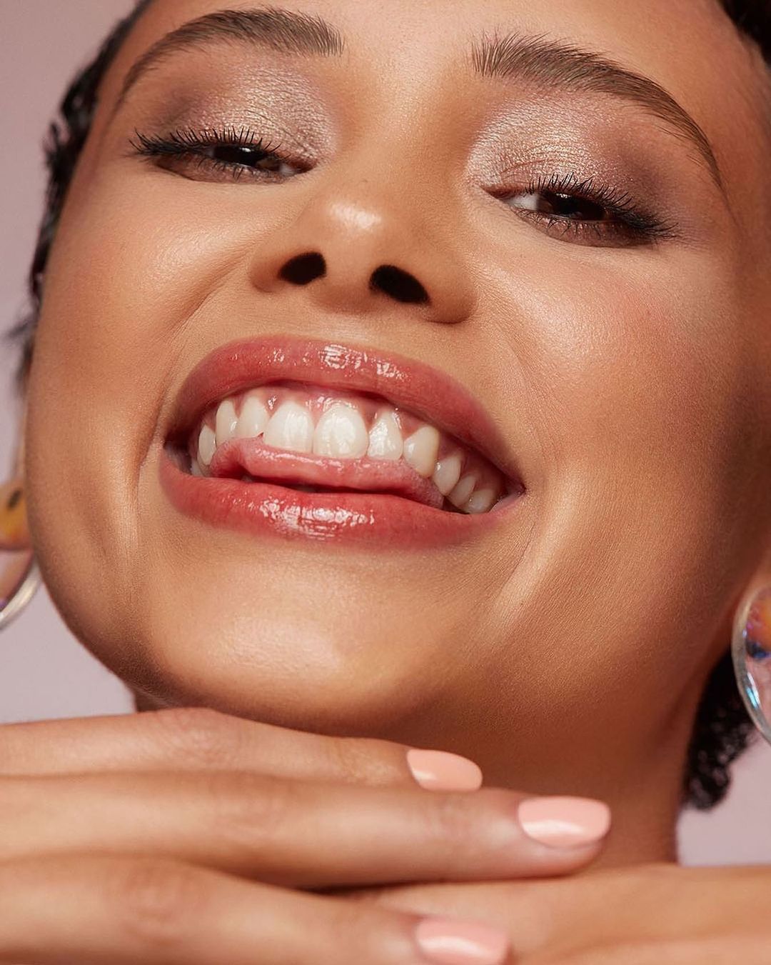 Close-up portrait of a smiling woman showing teeth with glossy pink lips and pastel orange manicured nails by photographer Jenn Collins.