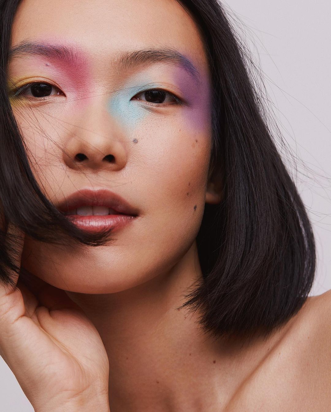 Close-up portrait of an Asian woman with colorful makeup around her eyes, fair skin, dark hair, and a neutral expression.