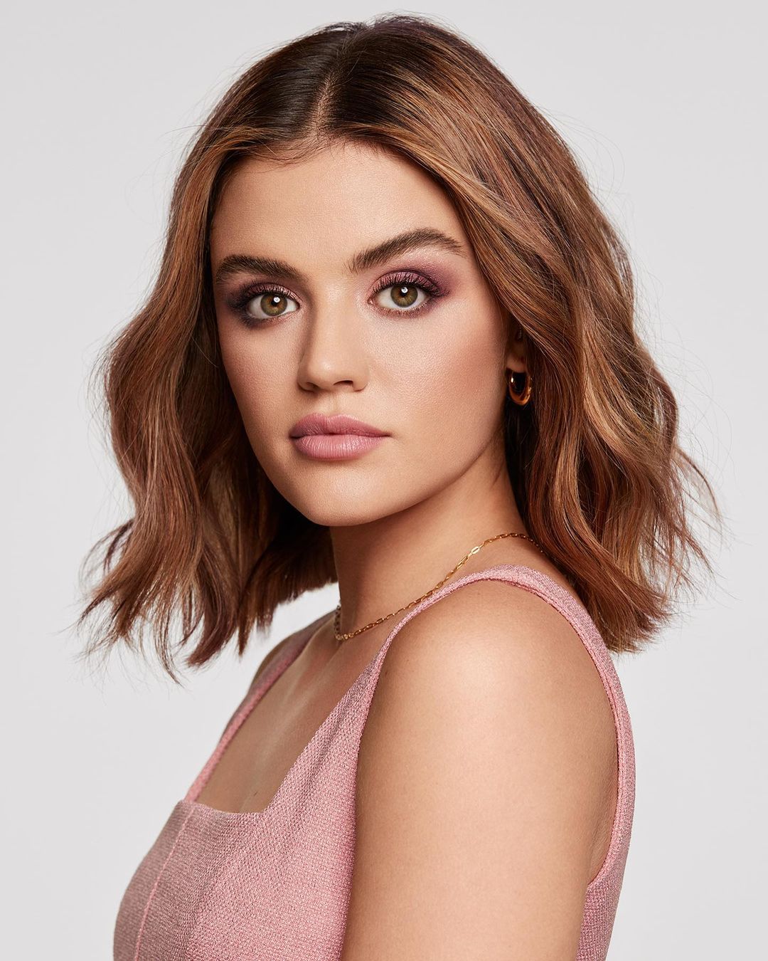 Close-up portrait of a brunette woman with fair skin and light pink lipstick in a sleeveless top against a neutral background.