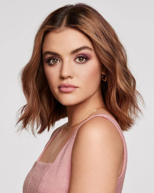 Close-up portrait of a brunette woman with fair skin and light pink lipstick in a sleeveless top against a neutral background.