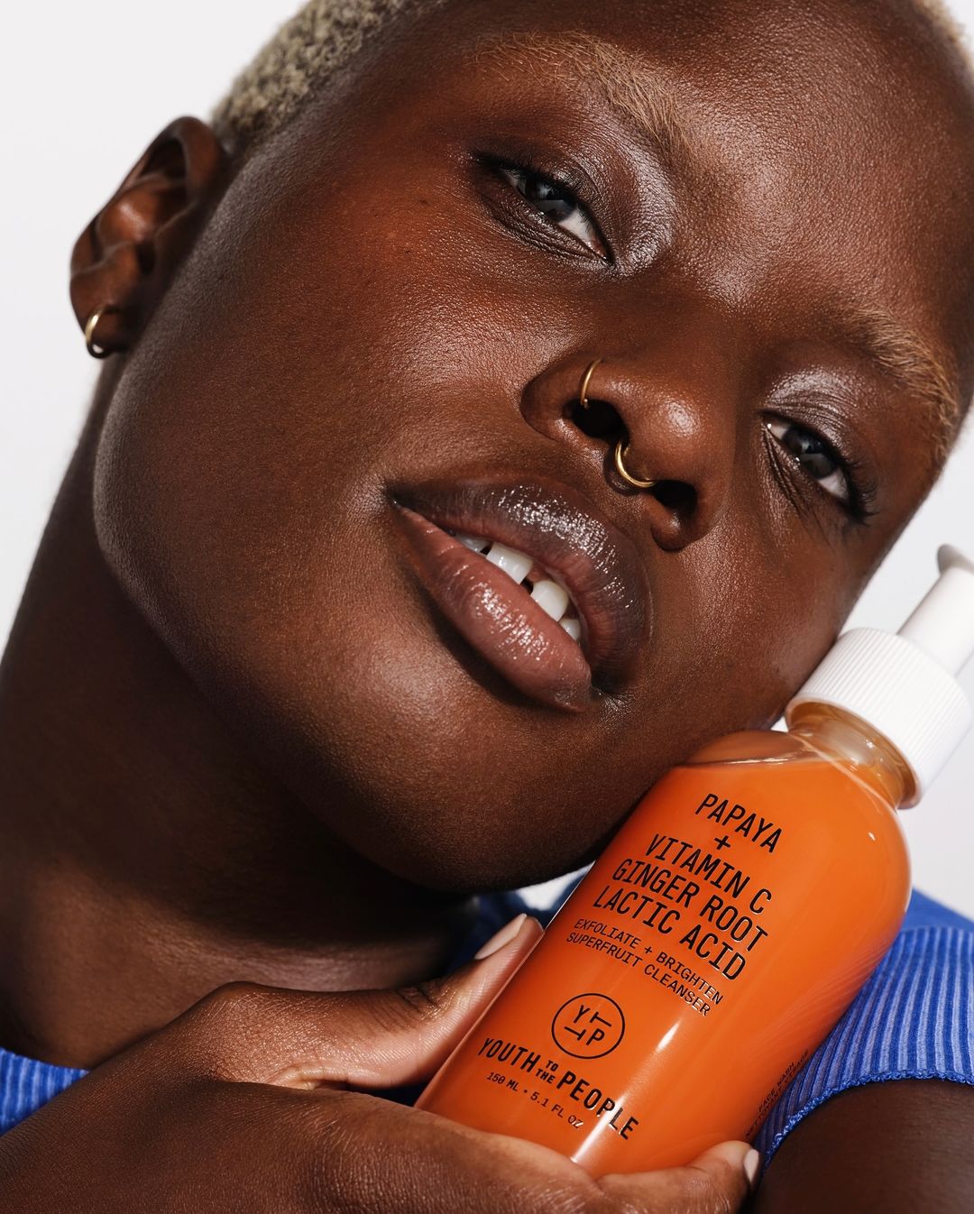 Close-up of a dark-skinned person with short blonde hair holding an orange bottle of Youth to the People Papaya + Vitamin C cleanser.
