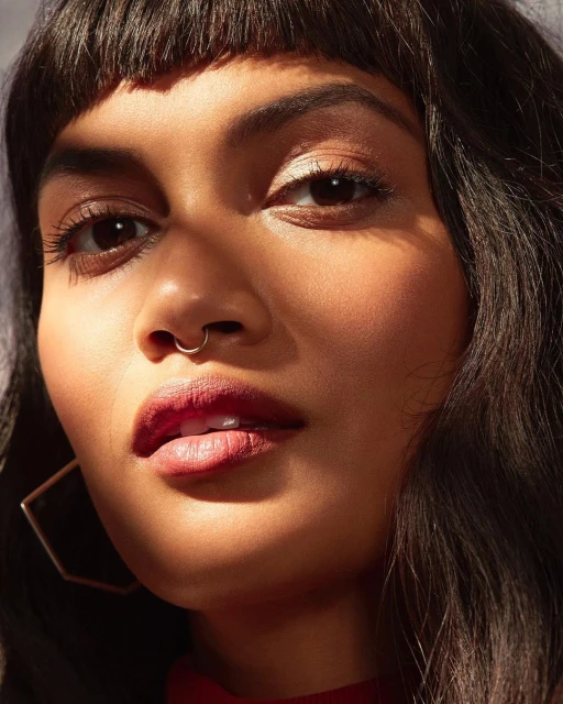 Close-up portrait of an adult female with dark hair and a septum piercing, illuminated by natural light casting shadows on her face.
