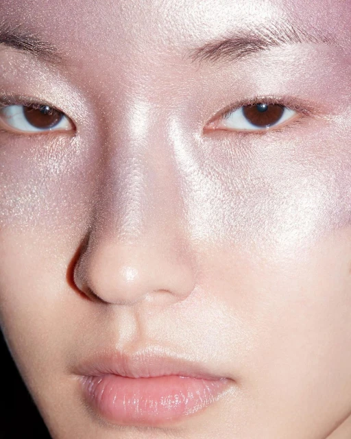 Close-up portrait of a woman with shimmery pink and white makeup on her face, including her eyelids and around her nose and lips.