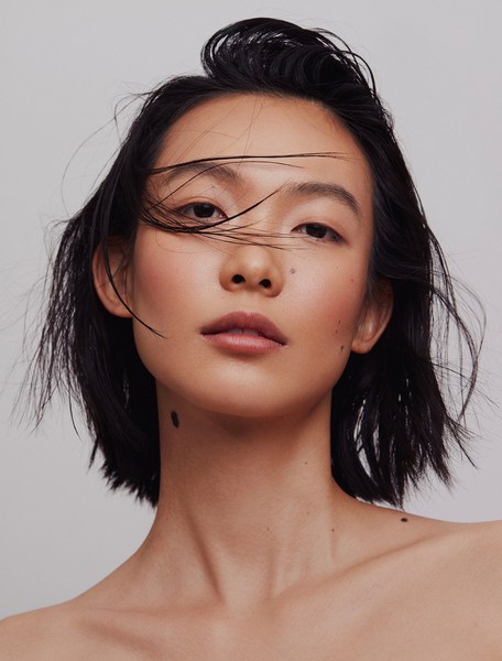 Close-up studio portrait of an Asian adult female with short dark hair, featuring soft lighting and a neutral backdrop, highlighting her natural makeup.
