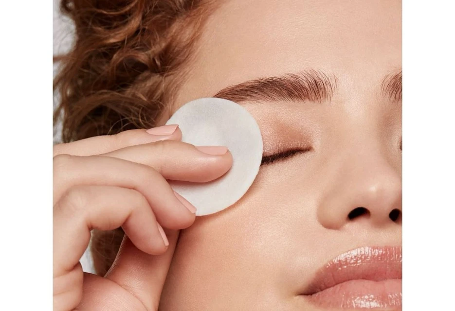 Close-up of a woman's face as she uses a cotton pad to remove eye makeup, showing skincare and beauty routine.