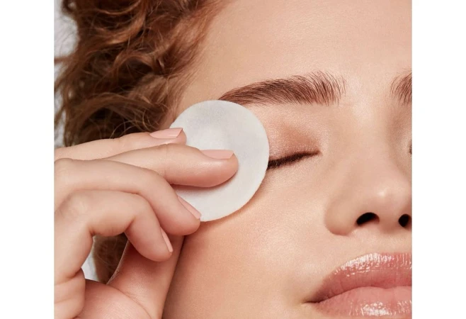 Close-up of a woman's face as she uses a cotton pad to remove eye makeup, showing skincare and beauty routine.