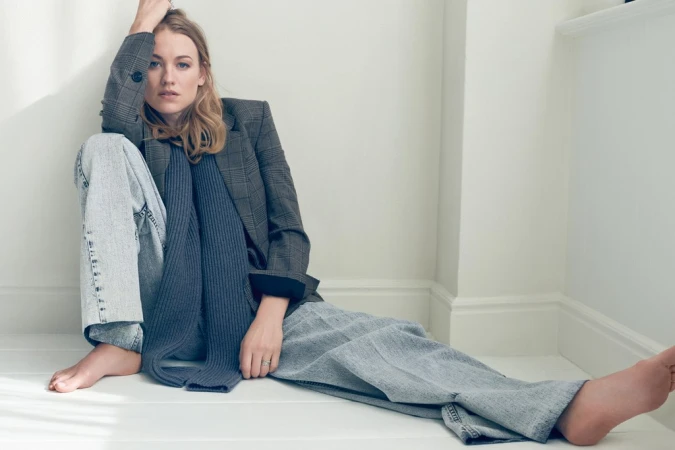 Woman in grey plaid blazer and blue jeans sitting on the floor against a white wall by photographer Kerry Hallihan.