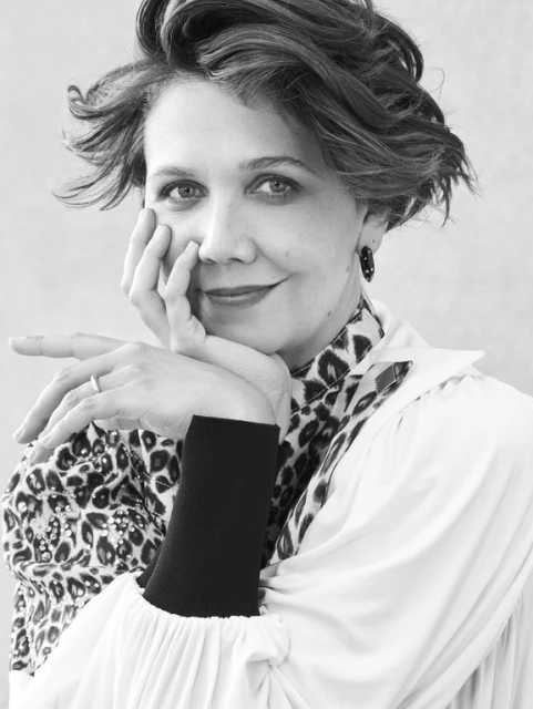 Black and white portrait of an adult woman with short curly hair in a print top and white jacket resting her face in her hands.