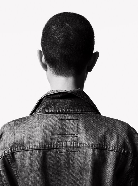 Back view of a person wearing a denim jacket against a white background. High contrast, black and white image.