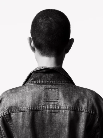 Back view of a person wearing a denim jacket against a white background. High contrast, black and white image.