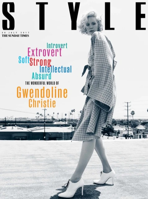 Fashion magazine cover featuring Gwendoline Christie in a checkered robe and heels, with a city skyline and a gray floor backdrop.